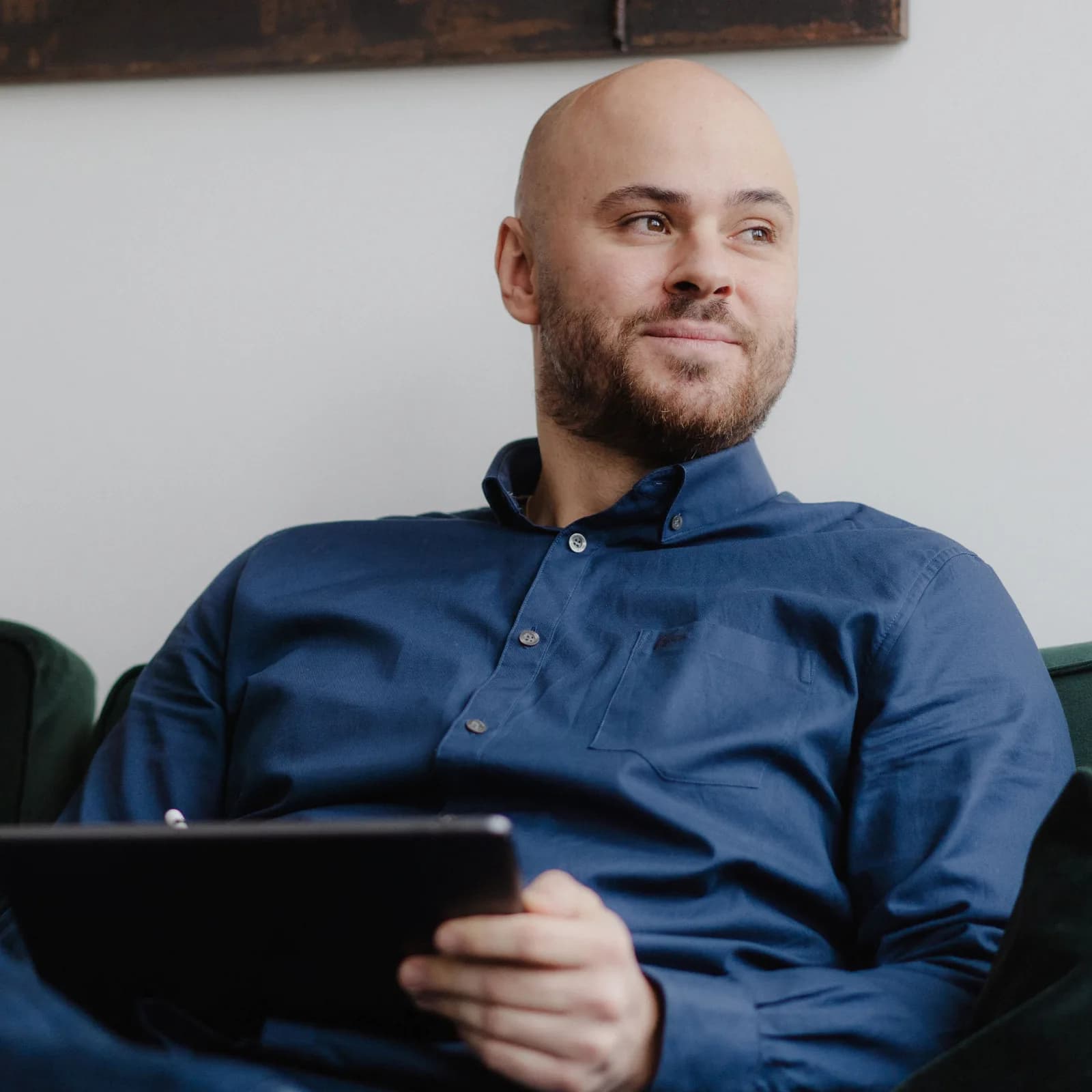 Anil Altinbasak sitzt mit einem Tablet in der Hand auf einem Sofa und denkt nach.